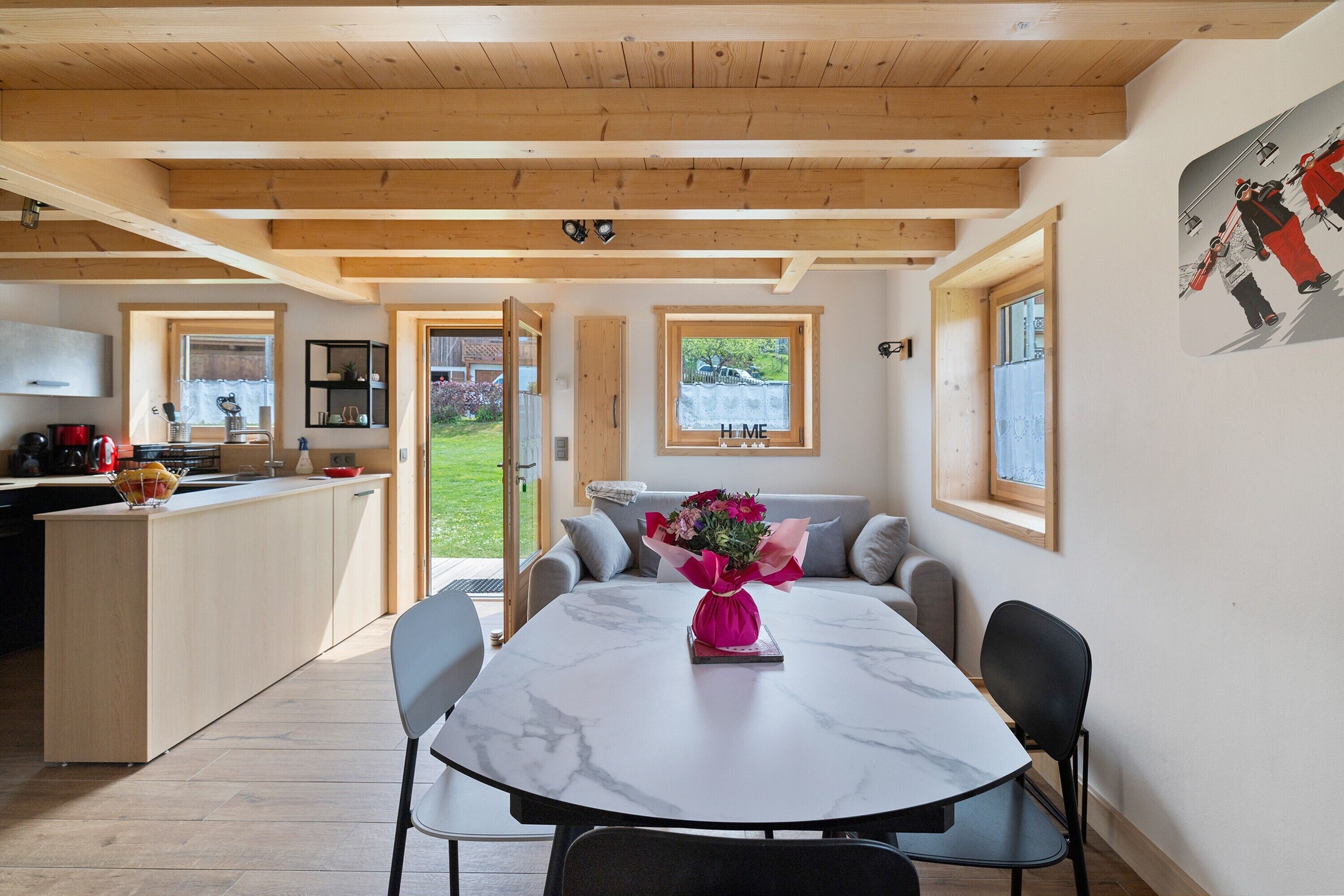 Une cuisine moderne avec des poutres en bois, un coin repas doté d’une table en marbre et une vue sur l’extérieur.