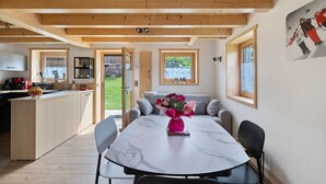 A modern kitchen with wooden beams, a dining area with a marble table, and a view of the outdoors.