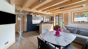 A modern interior with a dining area, kitchen, and living space, featuring wooden beams, a flat-screen TV, and a sofa.