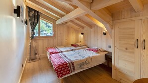 A wooden cabin with two beds, a wardrobe, and a window with curtains.