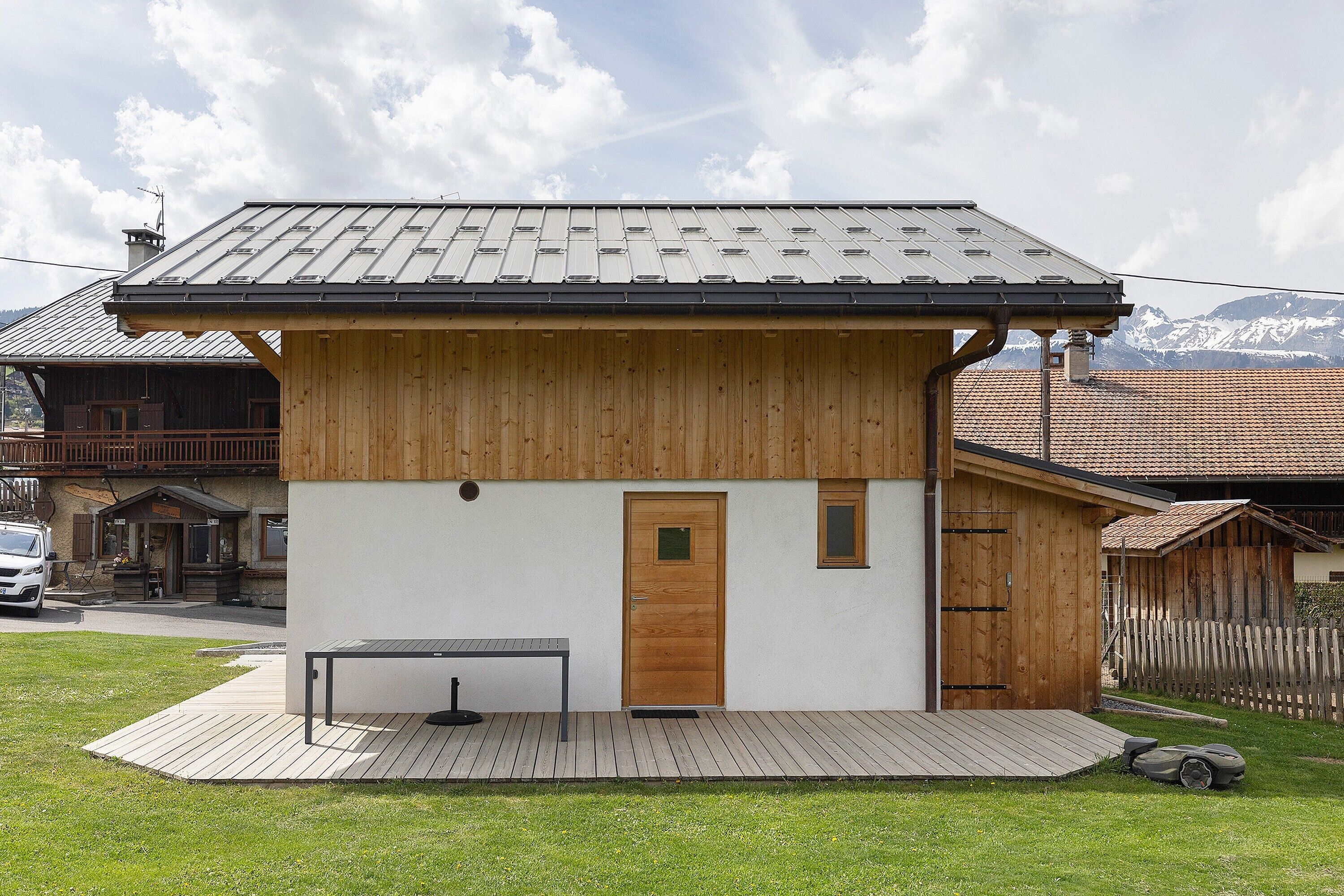 Une petite maison en bois avec un toit en métal, une porte et une petite table à l’extérieur.