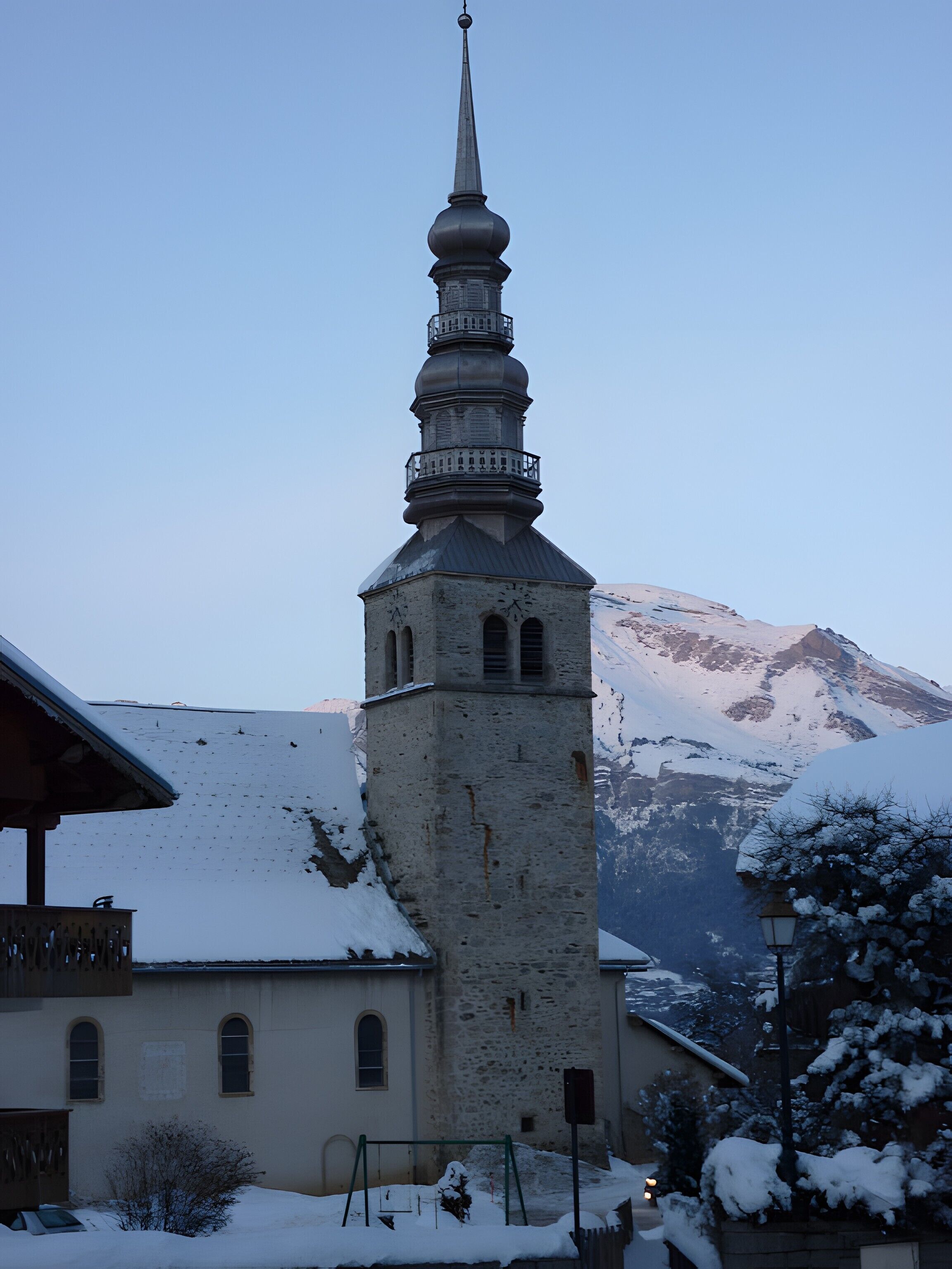 En kyrka med ett högt klocktorn, ett snötäckt berg i bakgrunden och en klar himmel.