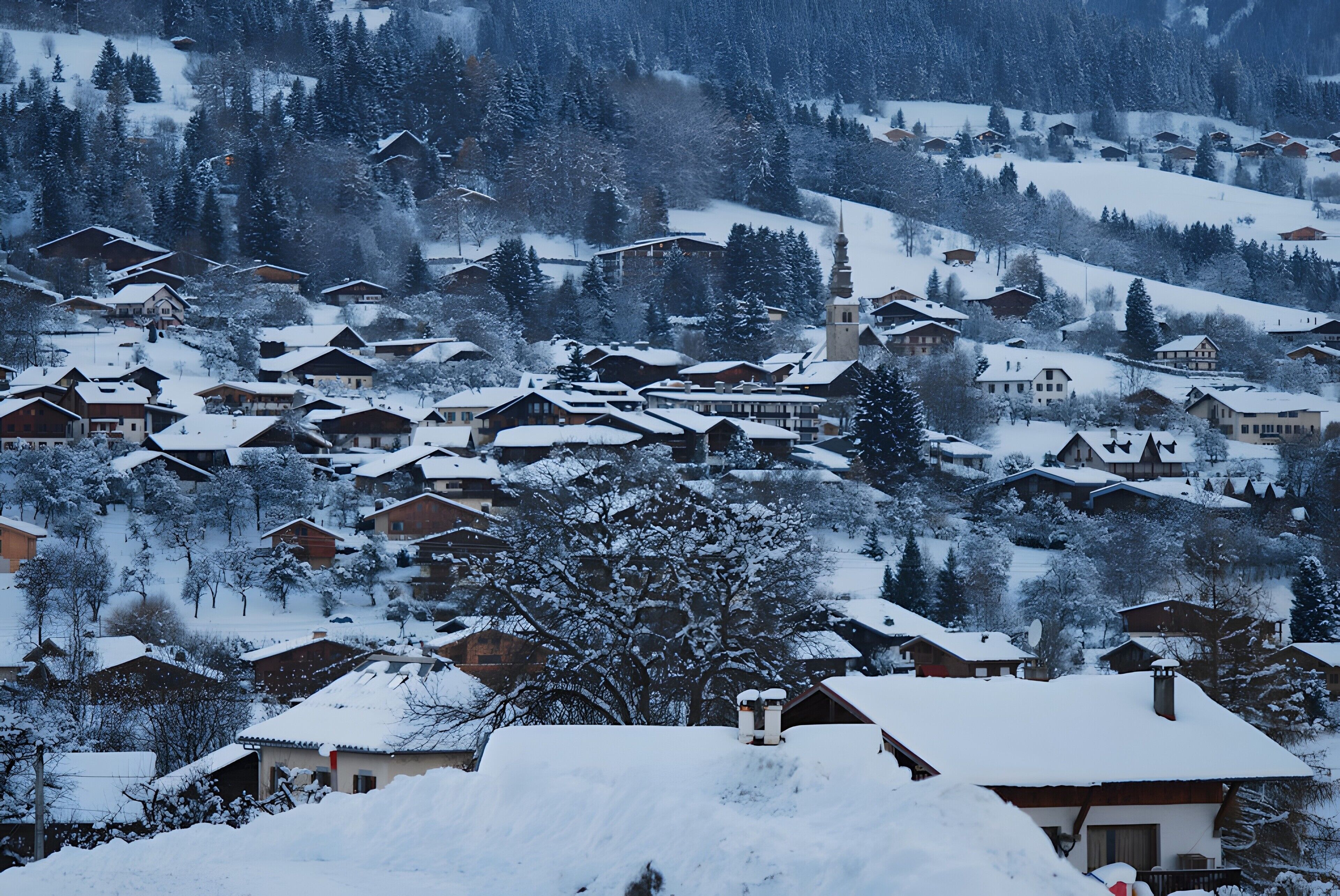 Un village enneigé, avec des maisons traditionnelles, une église et une colline en arrière-plan.