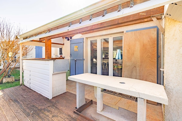 Un espace extérieur abrité, doté d’une terrasse en bois, d’un banc blanc et d’une petite structure en bois.