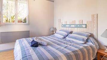 Un dormitorio con cama, ventana, cartel en la pared, mesita de noche y lámpara.