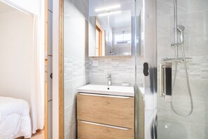 Une salle de bain moderne avec une douche à l’italienne en verre, un lavabo blanc avec un meuble en bois, et un miroir au-dessus du lavabo.