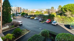 Een parkeerplaats met meerdere auto's, omgeven door groen en gebouwen op de achtergrond.