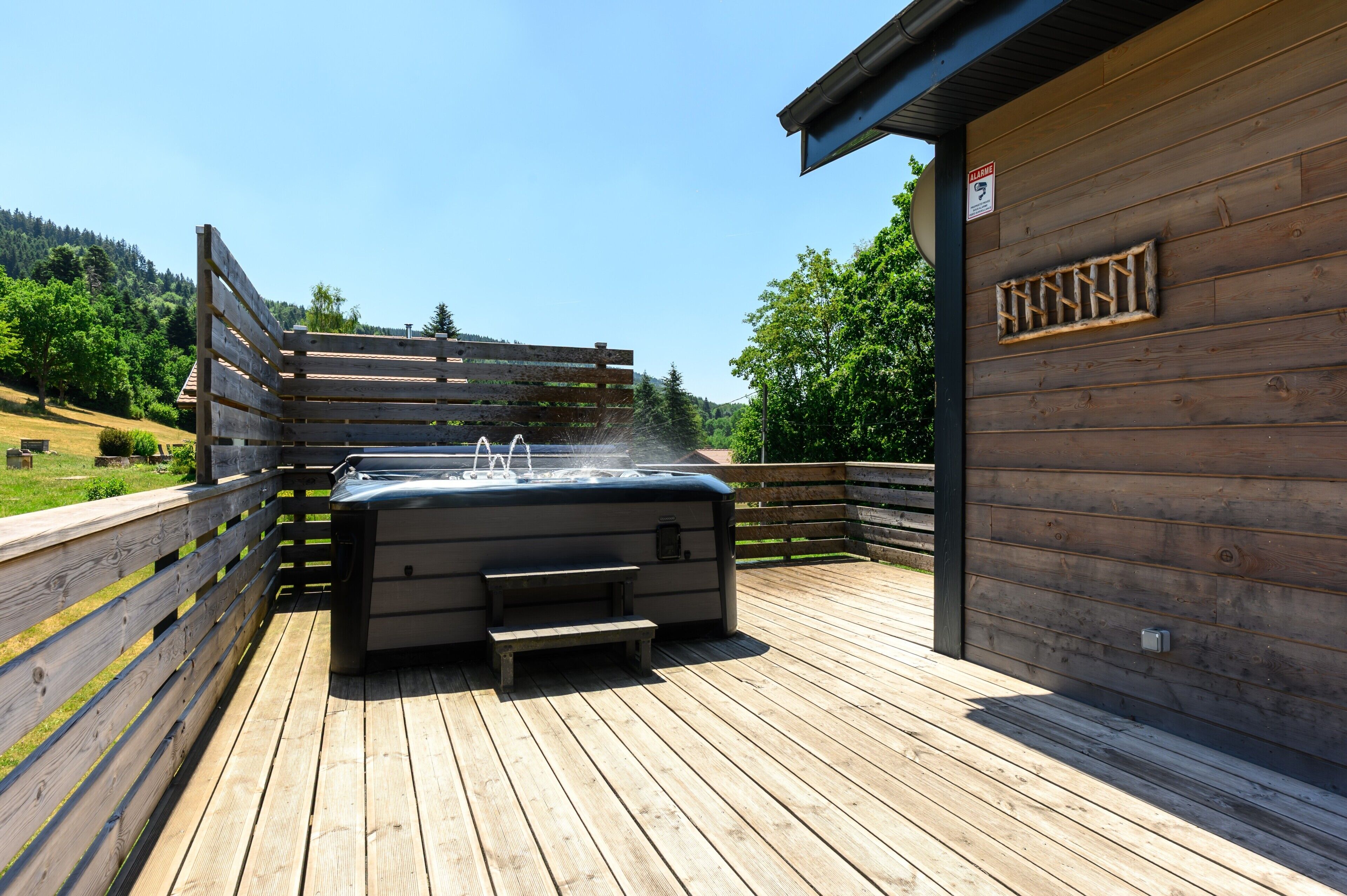A hot tub on a wooden deck with a wooden fence and a building in the background.