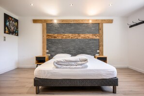 Une chambre moderne avec un grand lit, une tête de lit en bois et un mur d’accent en pierre.
