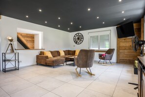 A modern living room with a sectional sofa, a rocking chair, a wooden staircase, and a ceiling fan. - Gîte Perce Neige: Spa, Gym, Near Gérardmer and Ski Slopes (Gerbépal)