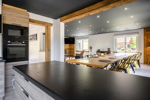 A modern kitchen with a large island, built-in oven, and dining area with chairs. - Gîte Perce Neige: Spa, Gym, Near Gérardmer and Ski Slopes (Gerbépal)