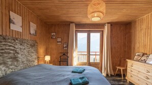 Um quarto de madeira com cama, cômoda, janela com vista e luminária pendente.