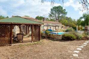 A covered outdoor seating area with a hammock, a pool, and a stone wall. - Roulotte o Bois d'mon cœur - Au Bois Joli (Bussac Forêt)