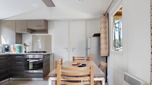 Une cuisine compacte dotée d’un four encastré, d’une table à manger avec des chaises et d’une fenêtre agrémentée de rideaux à motifs.