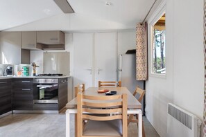 A compact kitchen with a built-in oven, a dining table with chairs, and a window with patterned curtains.