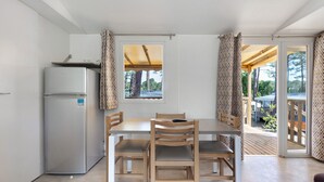 Une cuisine compacte équipée d’un réfrigérateur, d’une table à manger en bois et de chaises, donnant sur une terrasse extérieure.
