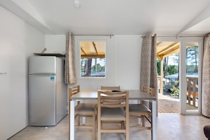 A compact kitchen with a refrigerator, wooden dining table, and chairs, leading to an outdoor deck.