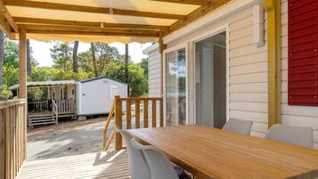 Une terrasse couverte avec une table et des chaises en bois, une plateforme et une vue sur une maison avec une porte rouge.