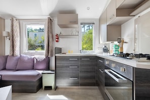 A modern kitchen with built-in appliances, a dining area with a sofa, and a window with curtains.