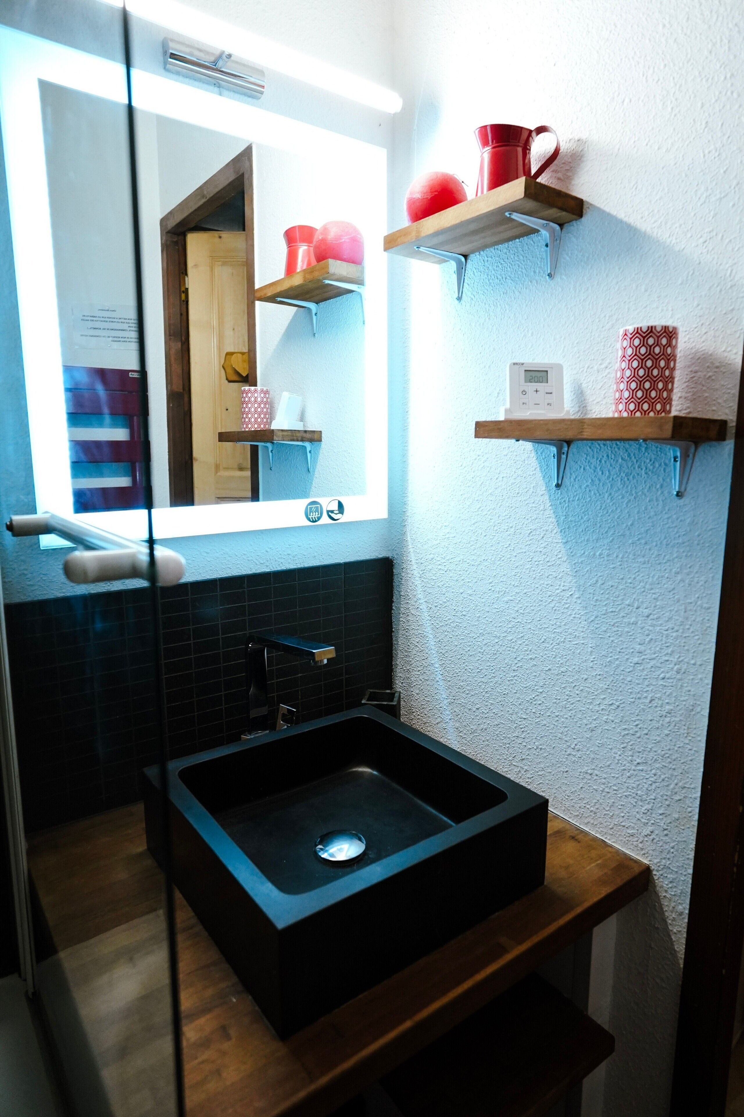 Un bagno con un lavandino nero, uno specchio e mensole in legno con tazze rosse e decorate.