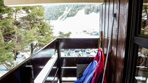 A balcony with a view of a snowy mountain, a wooden railing, and a pair of skis leaning against the wall.