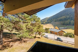 A view from a window overlooking a forested area with a building and a road. - Cozy Nest La Norma Les Campanules (Villarodin-Bourget)