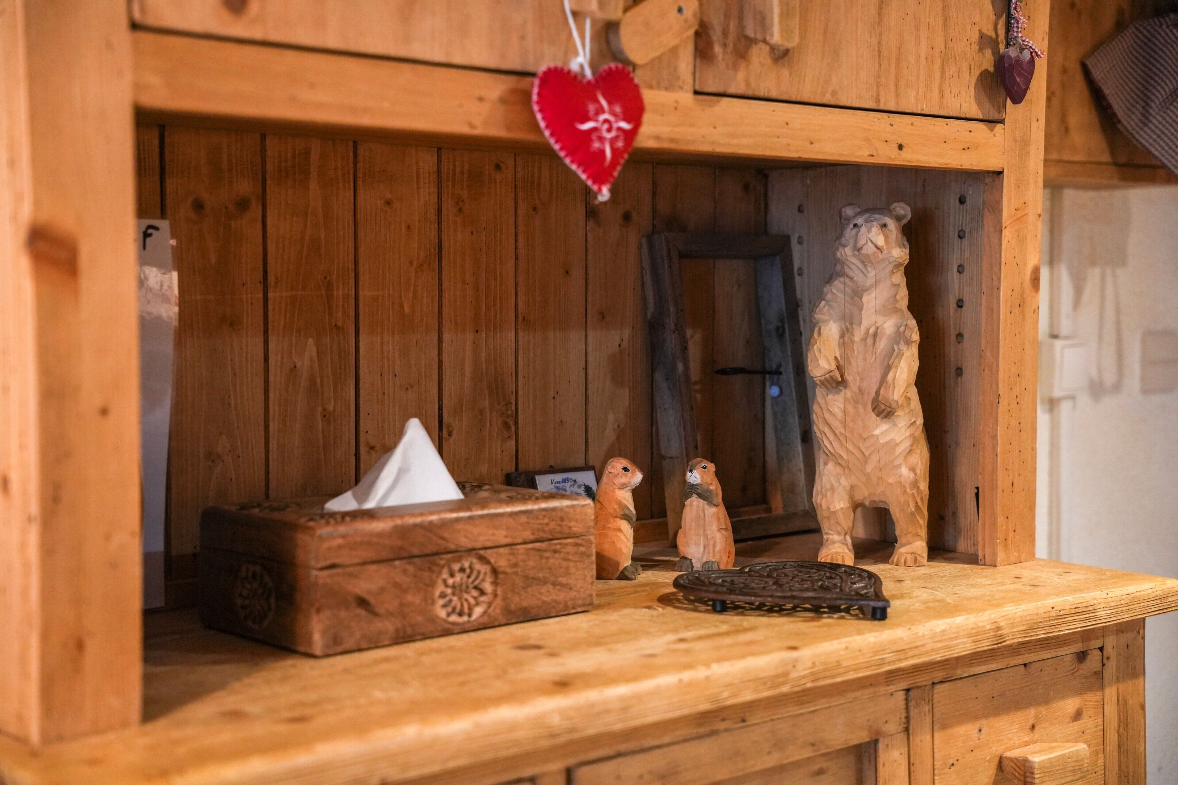 Uno scaffale in legno con una scatola di fazzoletti, una figurine di un orso intagliato e un ornamento a forma di cuore.