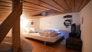 A cozy attic bedroom with a wooden ceiling, a single bed with white bedding, a television on a wooden crate, and a 'Bienvenue' sign on the wall.