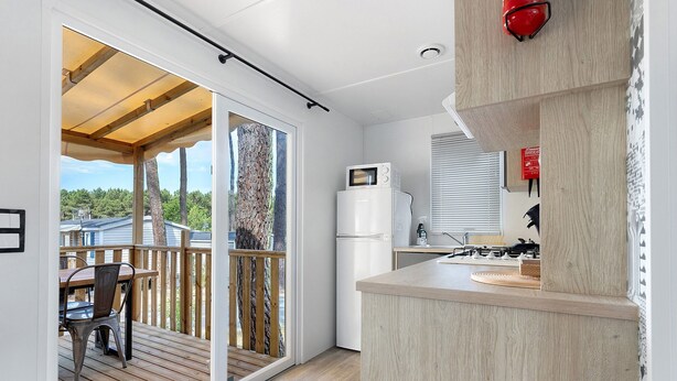 Une cuisine moderne dotée d’un four à micro-ondes encastré, d’une terrasse en bois et d’une porte-fenêtre coulissante donnant sur un espace extérieur.