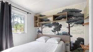 Une chambre à coucher avec un lit, une fenêtre avec des rideaux, une étagère fixée au mur et une fresque représentant des arbres.