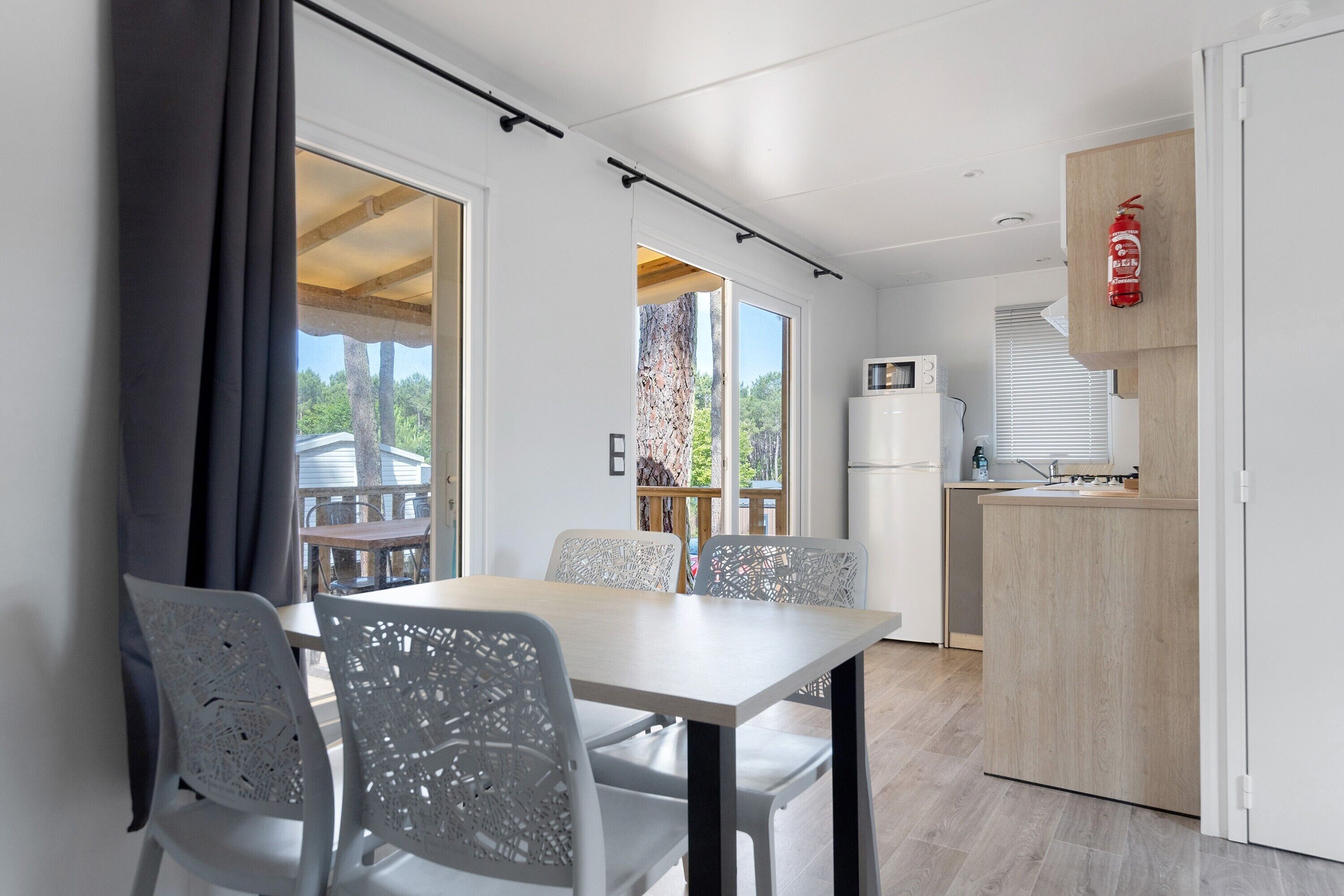 Een moderne keuken met een magnetron, een spoelbak en een houten kast. Er is een eethoek met een tafel en stoelen.