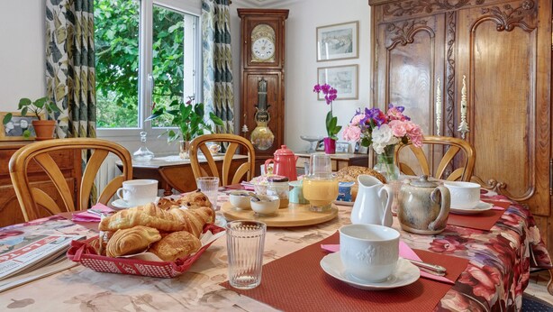 Ein Esstisch, gedeckt mit Frühstücksgebäck, einer Uhr und einer Blumenkomposition.