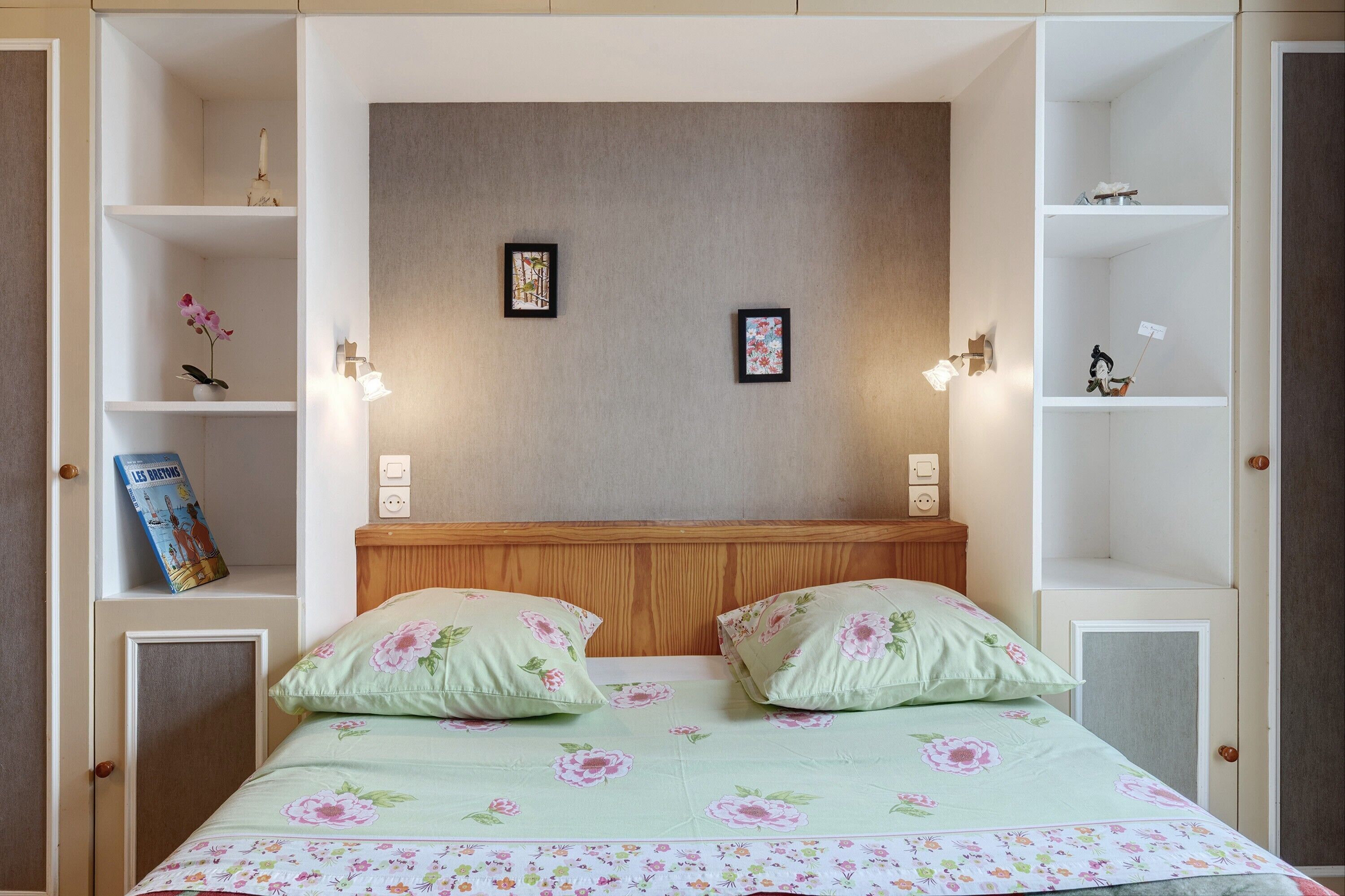 Ein Schlafzimmer mit einem Bett, zwei Kissen, einem Holz-Kopfteil und Wandregalen mit Dekoration.