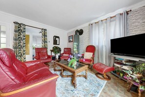Un salon avec des canapés en cuir rouge, une table basse en verre, un fauteuil rouge, un téléviseur et une bibliothèque remplie de livres.