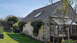 Une maison en pierre avec un toit en pente, une serre en verre et un jardin bien entretenu.