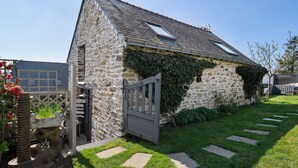 Un bâtiment en pierre doté d’un toit en pente, d’une porte en bois et d’une pelouse bien entretenue, agrémentée de pierres plates servant de pas japonais.