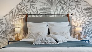 Un lit avec une tête de lit grise, des oreillers blancs et un plaid bleu. Il y a deux tables de chevet avec des lampes et des objets décoratifs.