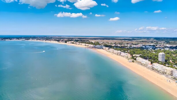 Un paysage urbain côtier avec une plage, des bâtiments et un ciel dégagé.