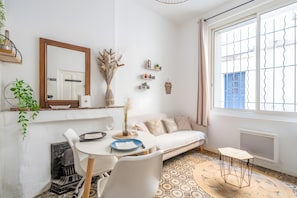 Una sala de estar moderna con sofá, mesa de comedor, sillas, un espejo, plantas decorativas y piso con diseño.