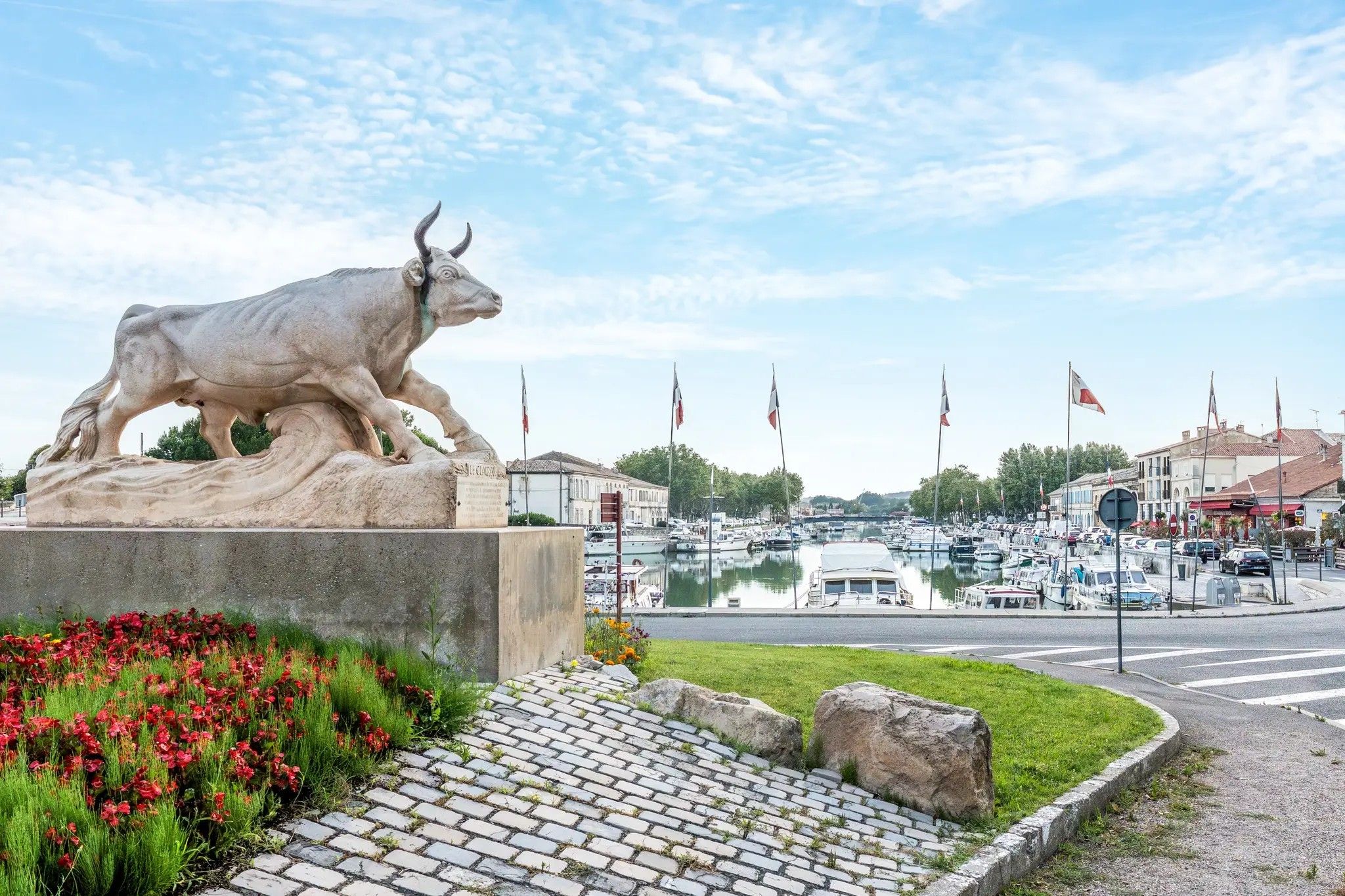 Eine Bullenstatue auf einem Sockel, im Hintergrund ein Yachthafen und Boote.