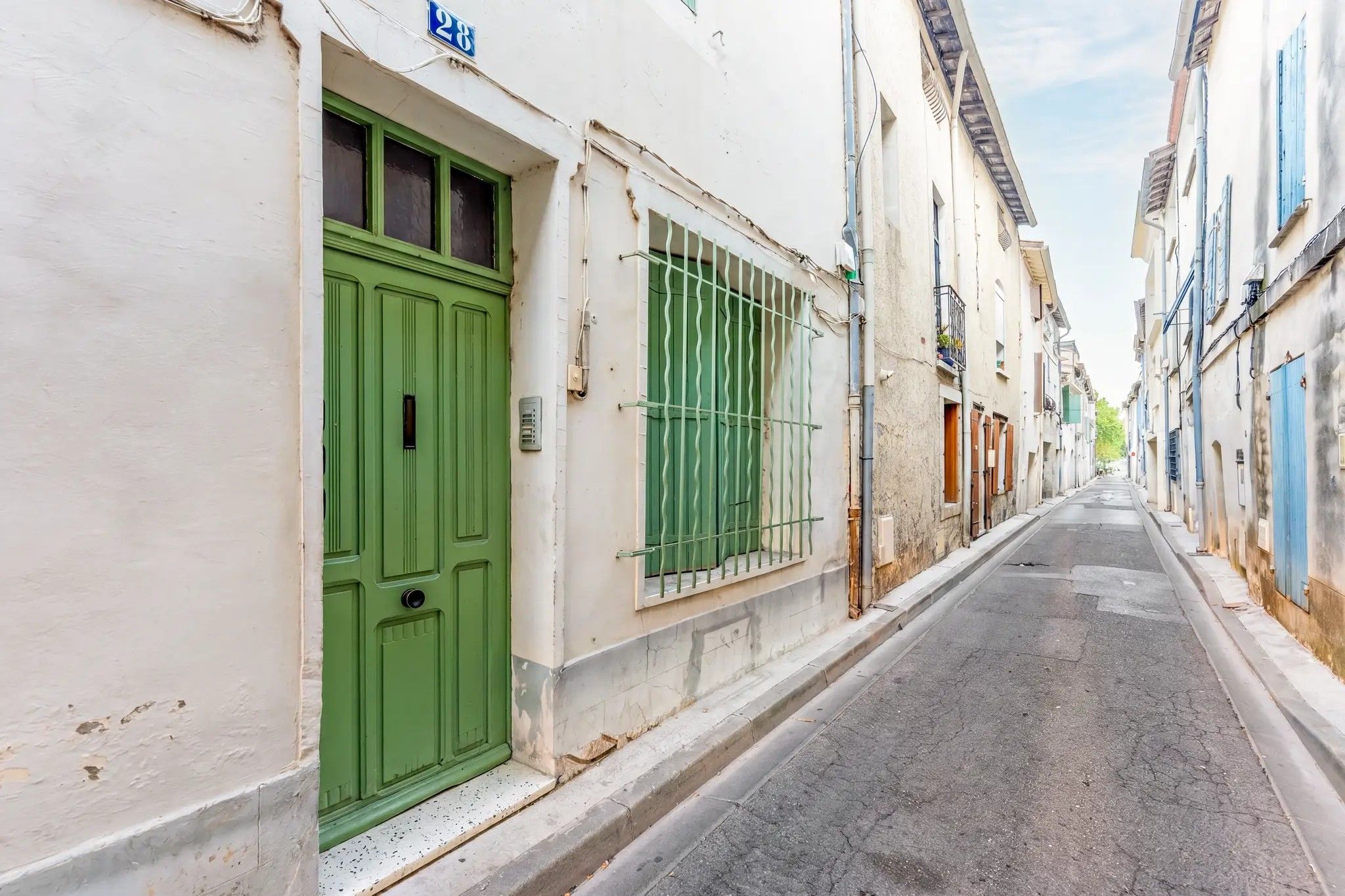 Rua estreita ladeada por edifícios com arquitetura tradicional, fachadas brancas e portas verdes.