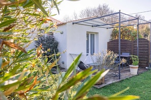 Ein Garten mit einer Pergola, einem kleinen Patio-Tisch und einem Topfpflanzen.