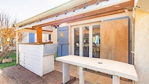 Un espace extérieur abrité, doté d’une terrasse en bois, d’un banc blanc et d’une petite structure en bois.