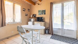 Une pièce avec une table blanche, deux chaises, un four à micro-ondes, un téléviseur et une porte-fenêtre coulissante avec des rideaux.