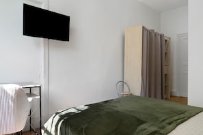 A bedroom with a bed, a television mounted on the wall, a chair, and a wardrobe.