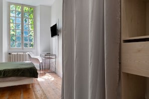 Une chambre à coucher avec un lit, un bureau, une télévision et une fenêtre donnant sur des arbres.
