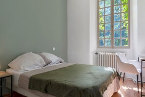 A bedroom with a bed, a radiator, a window with a view of trees, and a chair.