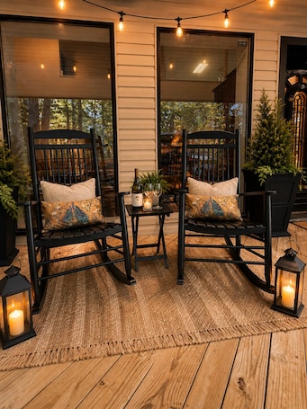 A cozy outdoor seating area with two rocking chairs, a small table with a candle, and string lights.
