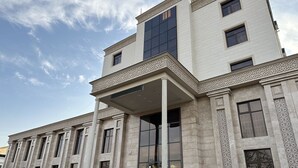 A large, multi-story building with a classical architectural style, featuring columns and decorative moldings. - Reikartz Grand Kokand (Kokand)