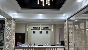 A reception desk with a sign reading "RECEPTION" and multiple flags. - Reikartz Grand Kokand (Kokand)